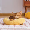 A fluffy yellow U-shaped cat sleeping pillow with neck support resting on a patterned cloth.