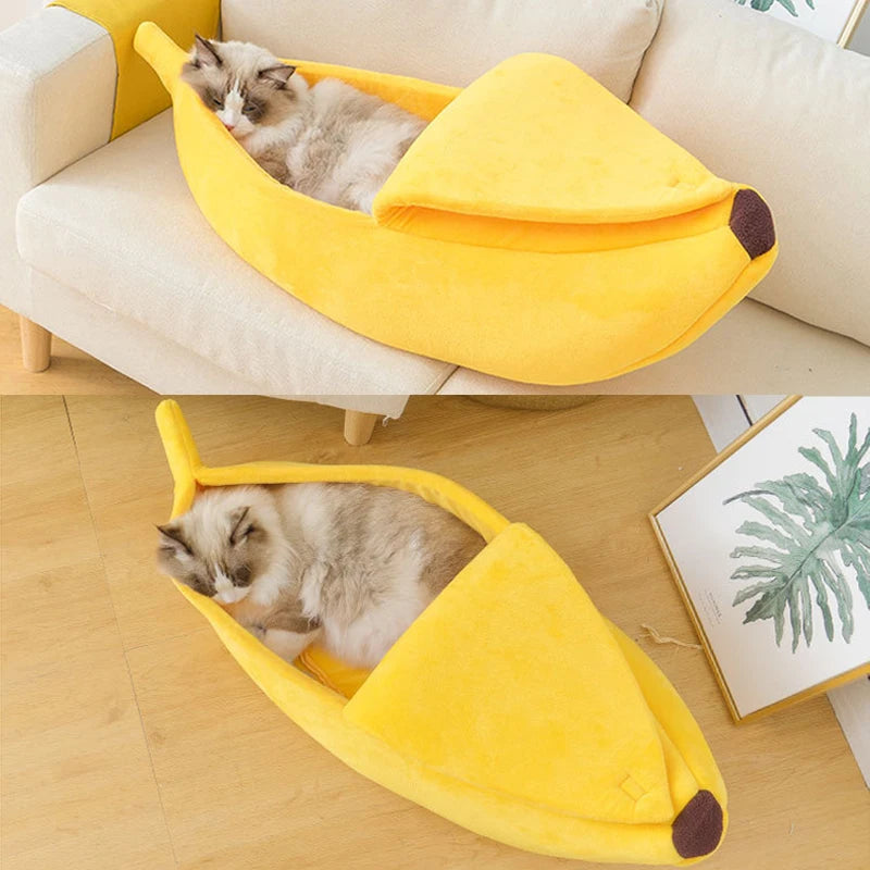 Un chaton gris et duveteux repose dans un lit pour animaux en forme de banane jaune vif sur un canapé clair.
