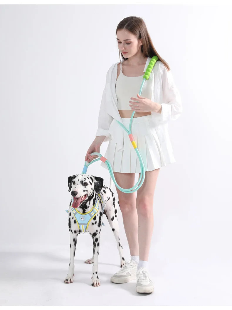 A woman holds an adjustable hands-free dog leash with a green and light blue cord, standing next to a dog.