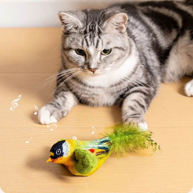 Eine tabbykat schaut auf ein grünes Federspielzeug auf einer Holzoberfläche.