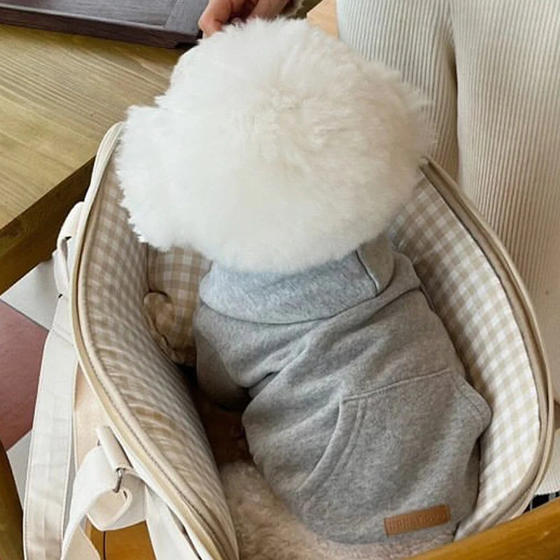 Un pull en polaire gris pour chien dans un panier tissé de couleur claire.
