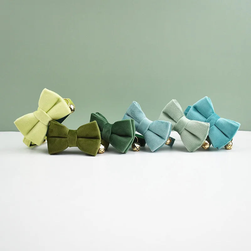 A row of elegant velvet cat collars in shades of olive green, teal, and mint green displayed on a white surface.