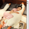 A woman is relaxing on a large white plush goose body pillow in a bedroom setting.