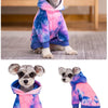 Un petit chien portant un sweat à capuche en polaire tie-dye rose, bleu et violet.