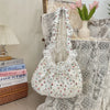 A white floral lace bowknot shoulder bag with a pleated design displayed on a table.