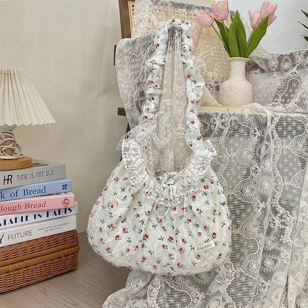 A white floral lace bowknot shoulder bag with a pleated design displayed on a table.
