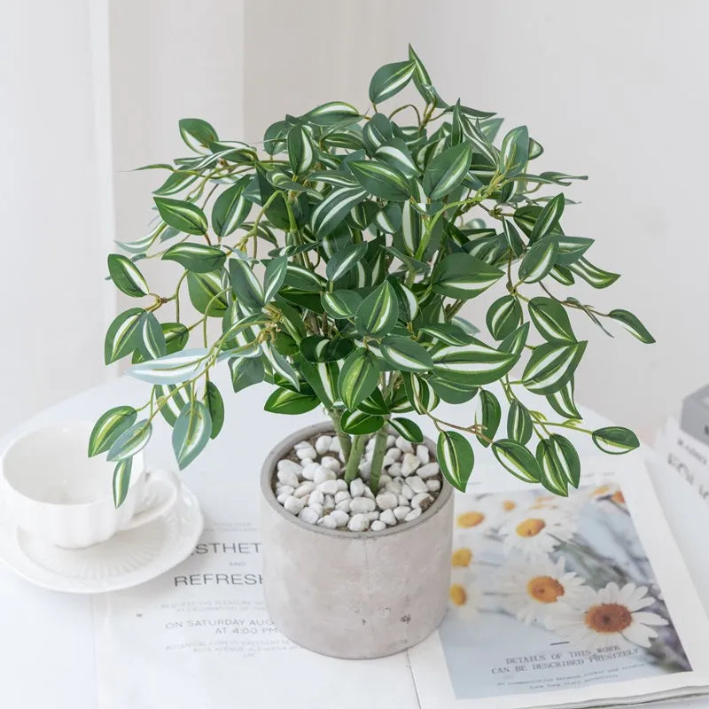 Artificial bonsai tree with green leaves in a pot displayed on a white surface.