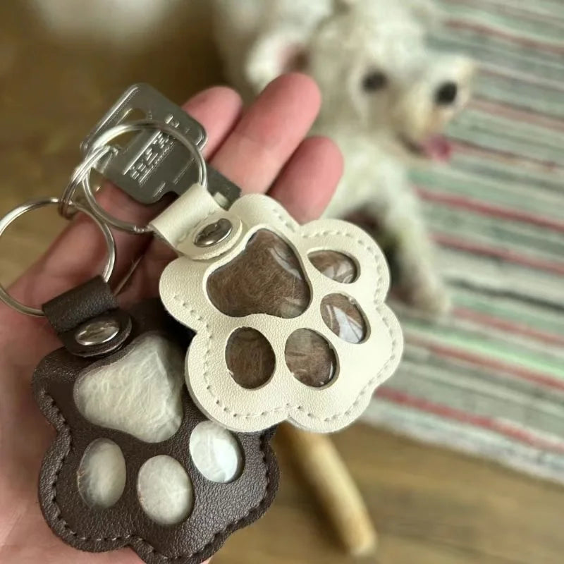 A leather paw print airtag keepsake with a cutout design is held in a hand next to a fluffy white dog.