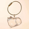 A clear glass keepsake box shaped like a cat, suspended by a braided gold-colored cord.