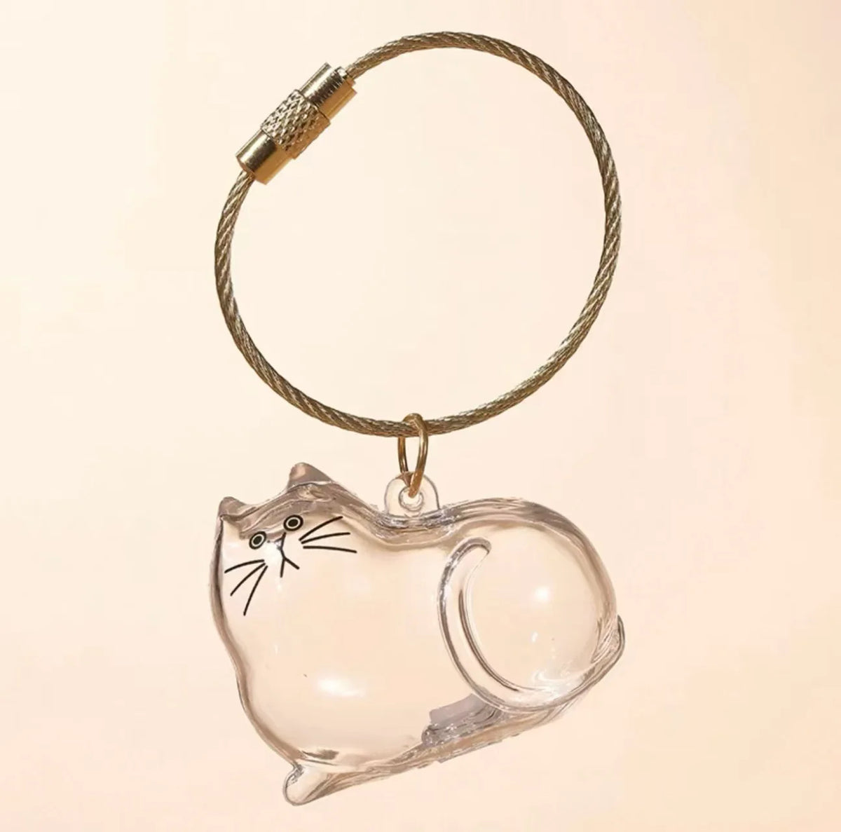 A clear glass keepsake box shaped like a cat, suspended by a braided gold-colored cord.
