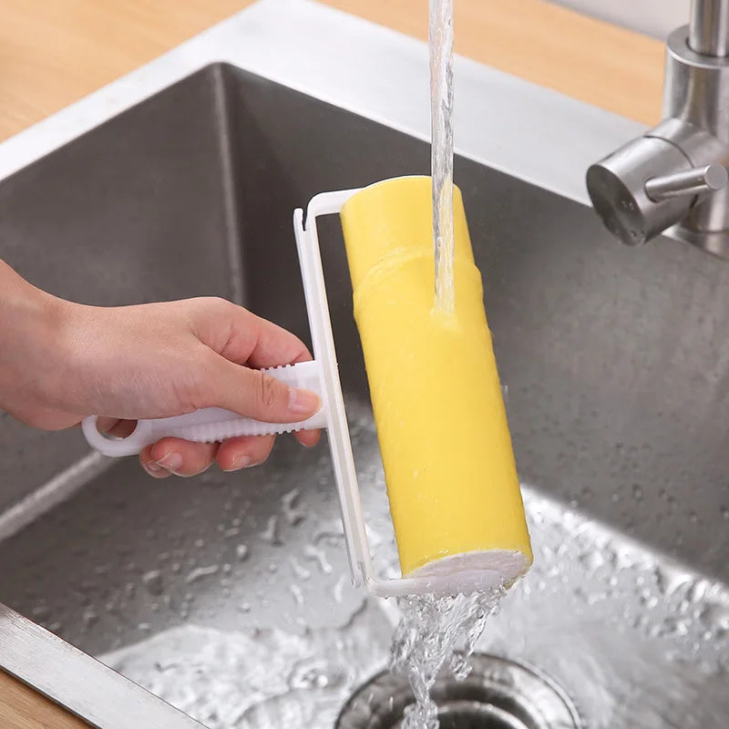 A hand is using a reusable lint roller to remove water from a yellow roll of the washable lint roller in a kitchen sink.