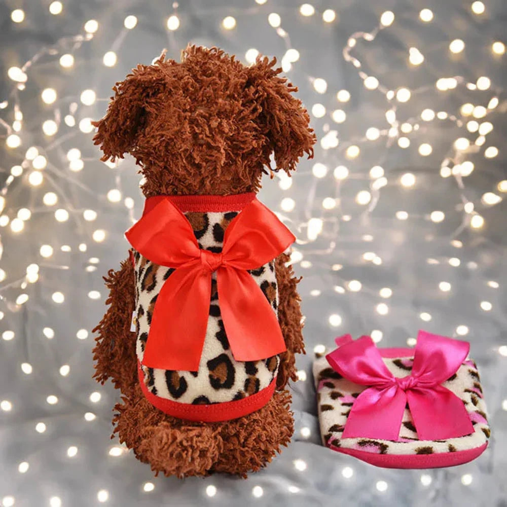 A brown, fluffy pet sweater with a leopard print body and an orange-red bow is displayed against a sparkling background.