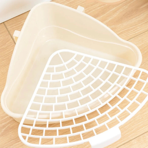 A white corner litter box with a removable mesh tray is shown on a wooden surface.