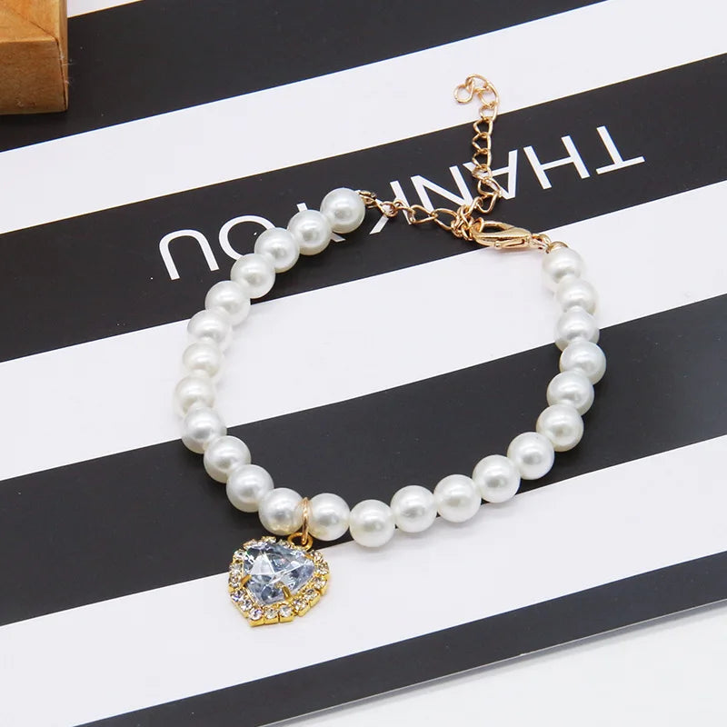 A delicate pearl necklace with a gold chain and a clear gemstone pendant displayed on a black and white striped background.