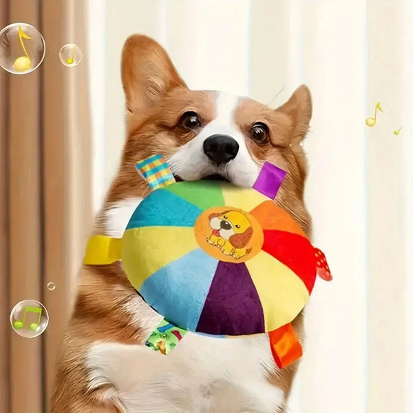 A brown and white dog holds a colorful, plush flying disc toy.
