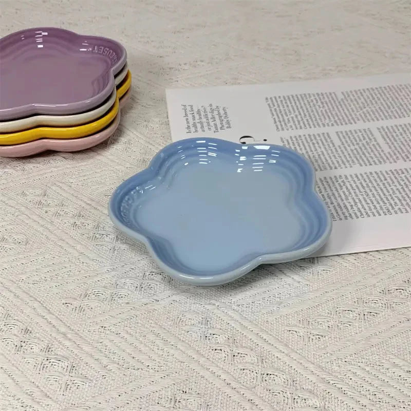 A light blue ceramic flower-shaped dipping dish is shown next to a stack of colorful pet bowls.