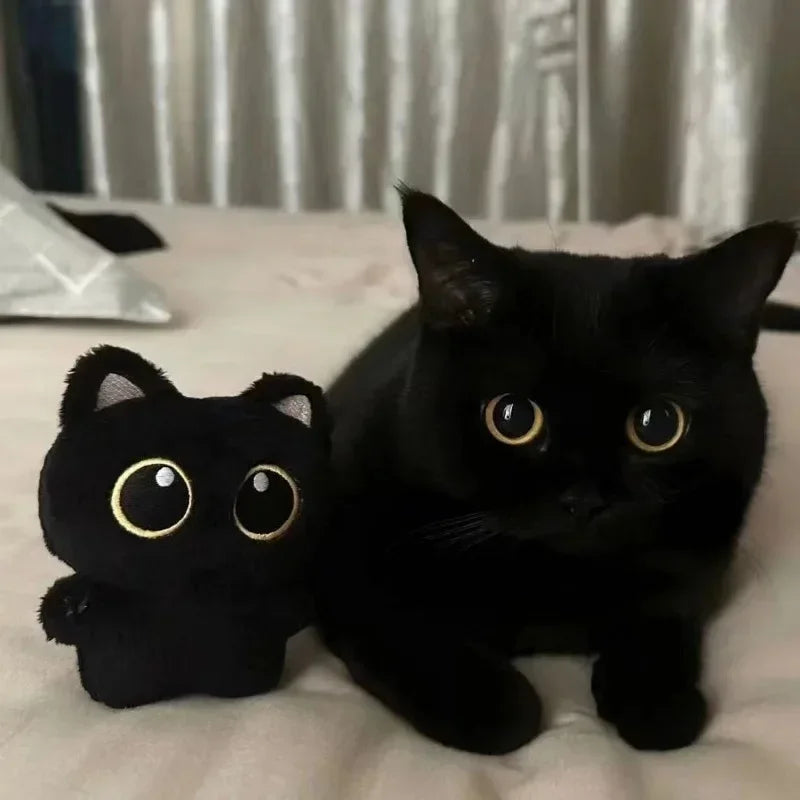 A small black cat plush pendant with gold eyes resting on a white surface.
