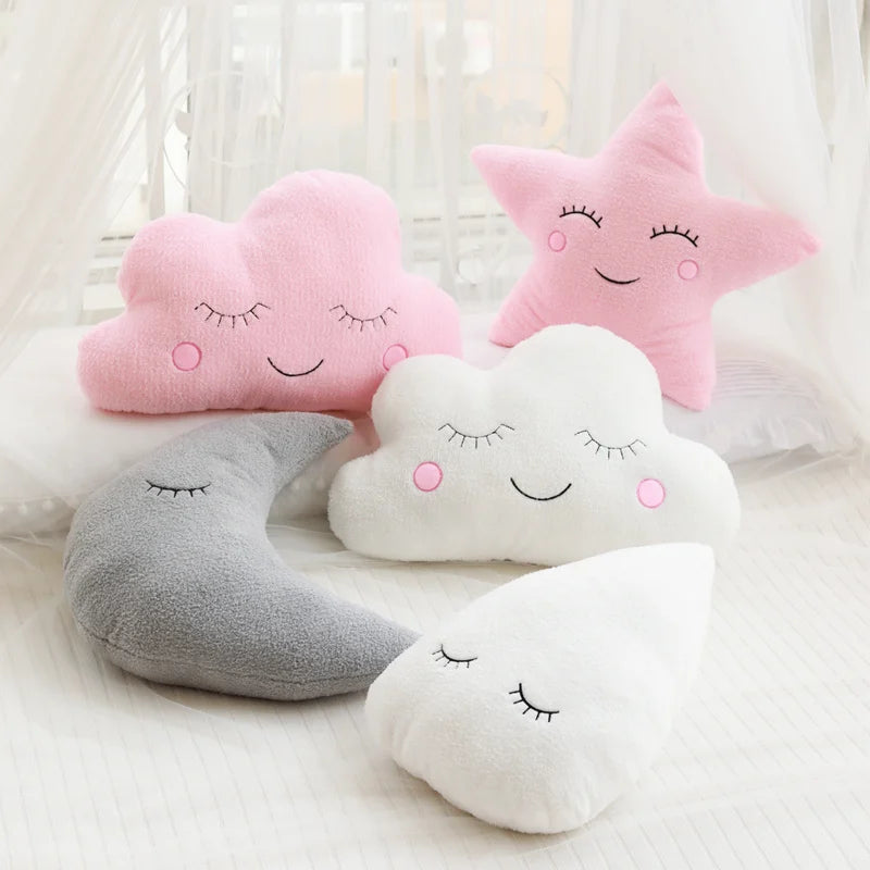 A collection of pink, white, and gray cloud and star shaped plush pillows arranged on a white surface.