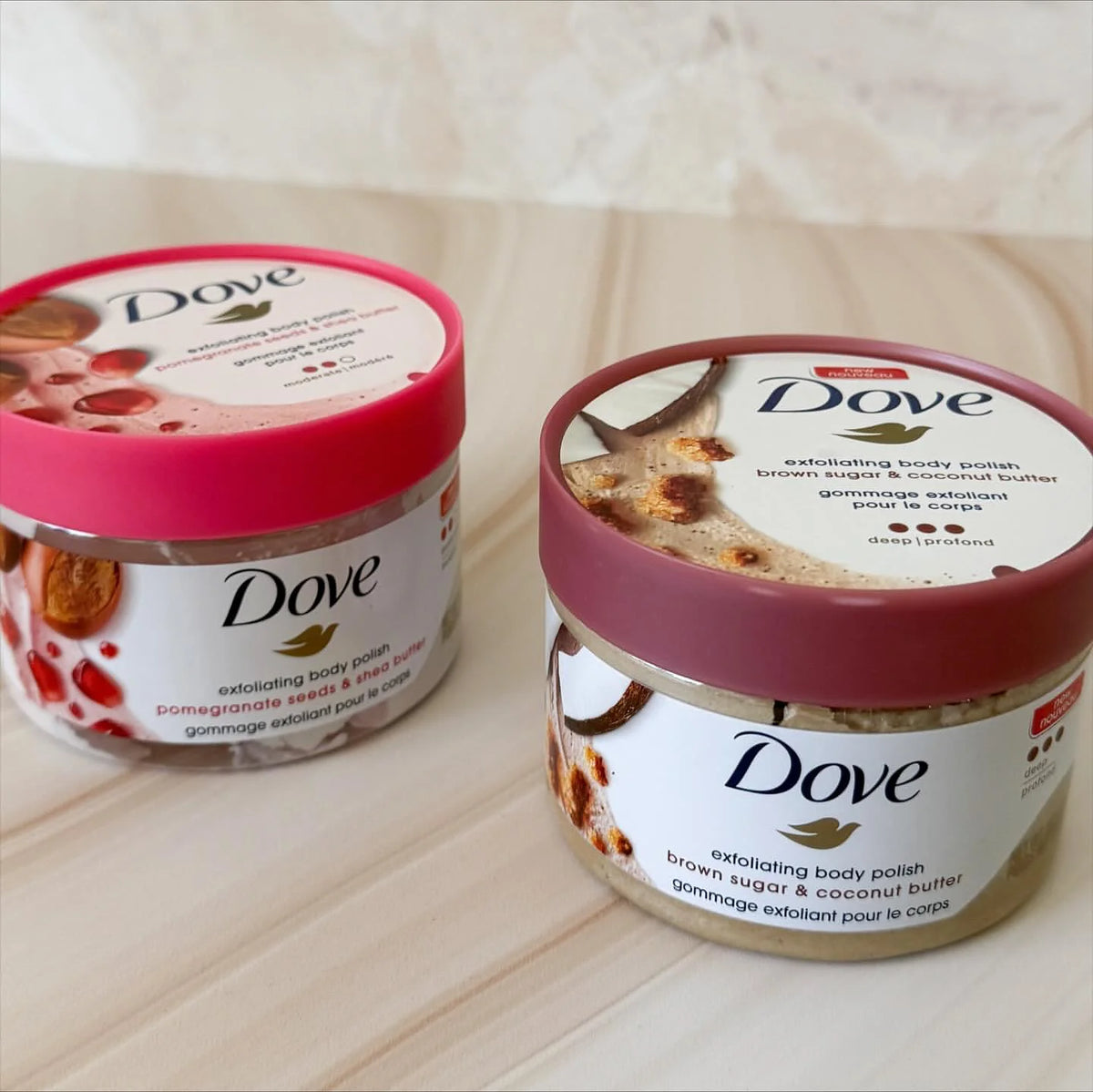 Two jars of Dove exfoliating body polish featuring brown sugar and coconut butter on a light wooden surface.