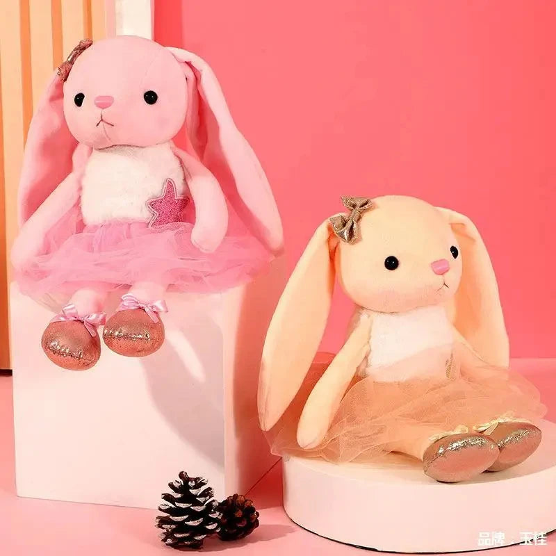 A pink plush rabbit stuffed animal toy with a pink tutu and a beige plush rabbit in a peach tutu.