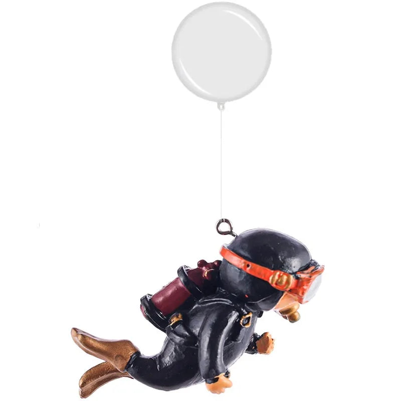 A resin mini diver aquarium ornament with a black helmet and orange accents is suspended by a white balloon string.