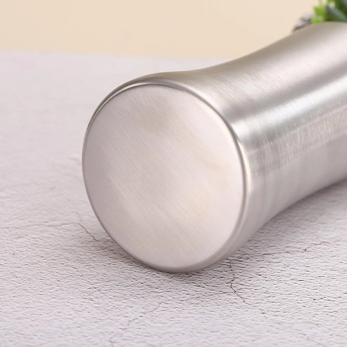 A silver, cylindrical portable dog water bottle with a built-in bowl resting on a white surface.