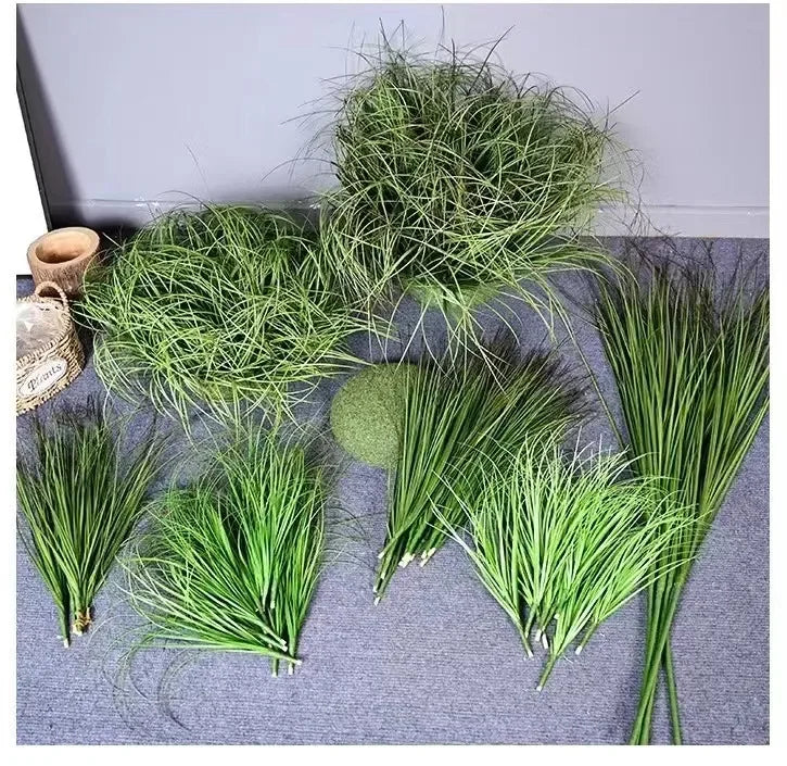 A collection of faux green grass, reeds, and onion grass bundles displayed on a gray surface.