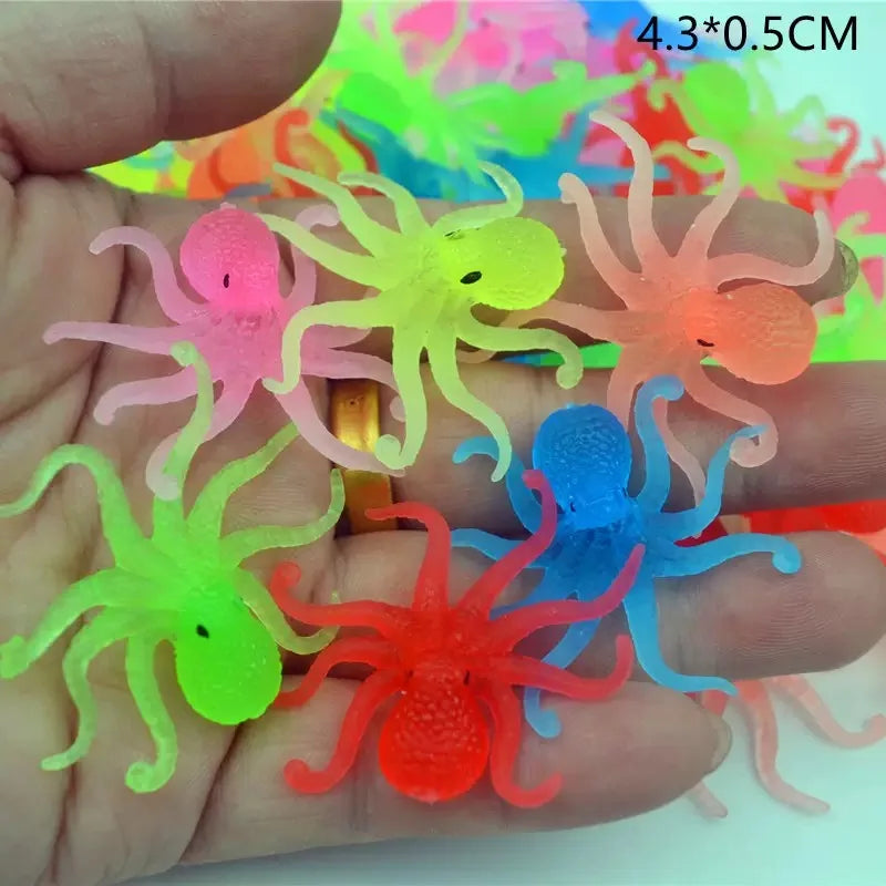 A hand holds a set of ten soft rubber goldfish bath toys in various colors including pink, yellow, green, orange, and blue.