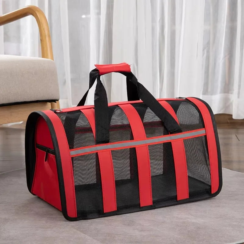 A red and black lightweight foldable mesh travel carrier bag for small pets resting on a gray surface.
