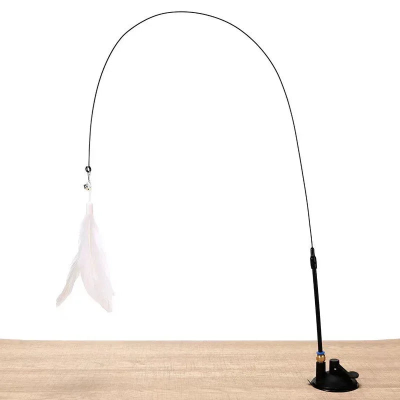 A long black feather wand toy with a suction cup and white feathers is shown against a wooden surface.