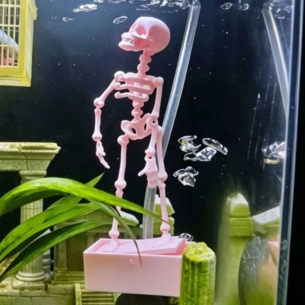 A pink dancing skeleton figure is displayed inside a glass aquarium with aquatic plants and decorations.