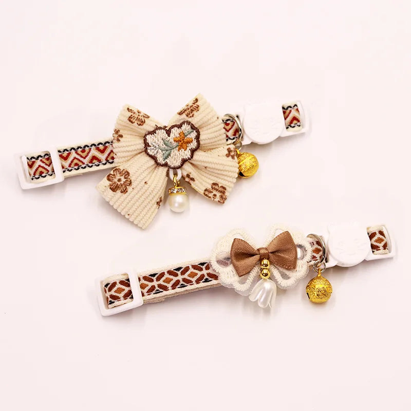 A beige breakaway cat collar featuring a floral bowknot and a gold bell.