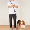 A person holds a black hands-free dog leash with a reflective stripe while standing.