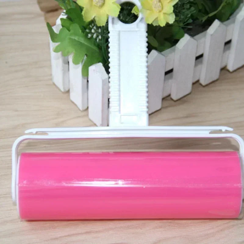 A pink reusable lint roller with a white plastic handle is shown in front of a white picket fence and yellow flowers.