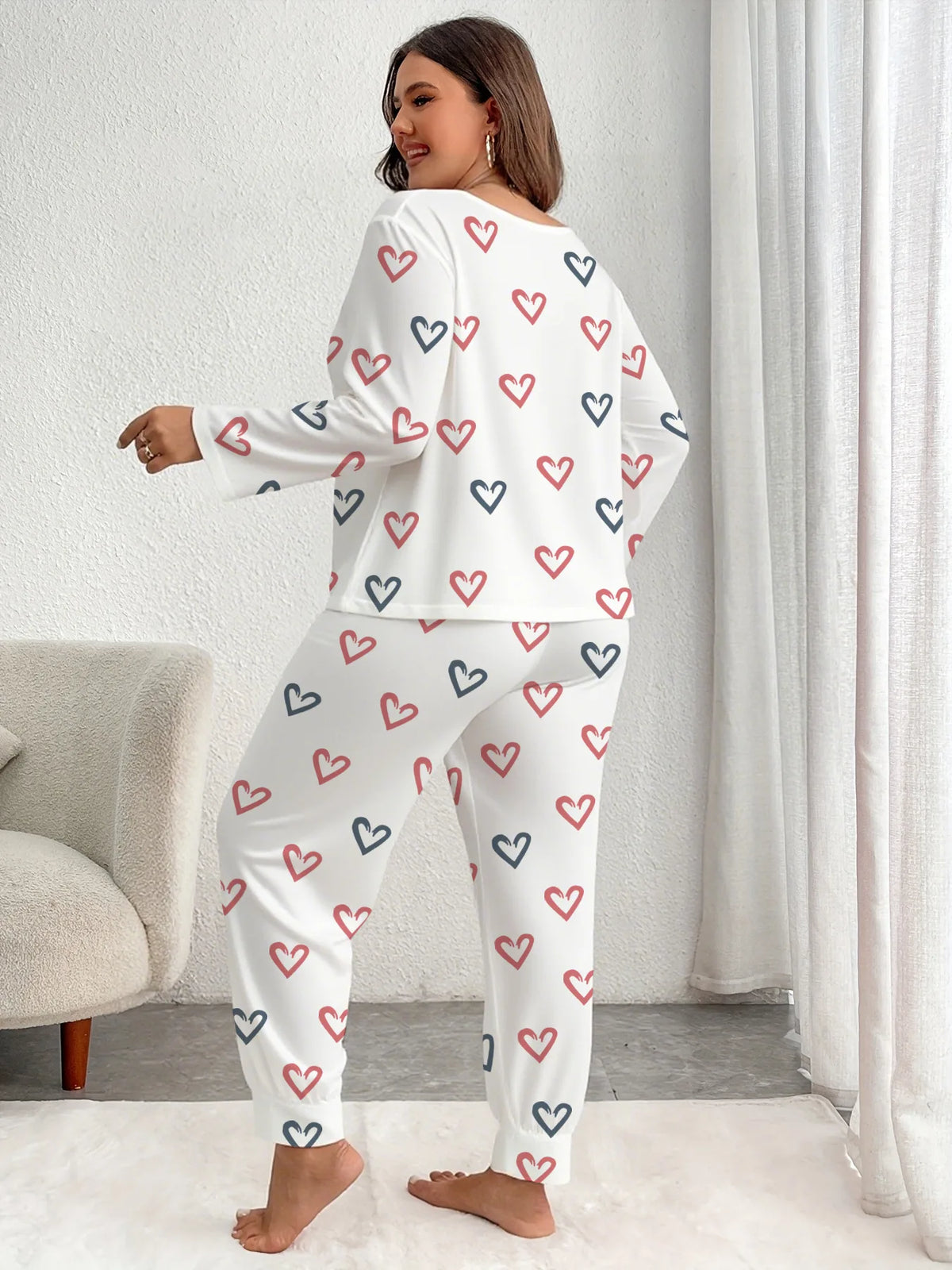 A woman models a white pajama set with a repeating pattern of red and blue hearts.