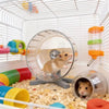 A hamster is running on a transparent exercise wheel inside a wire cage.
