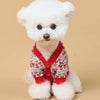 A fluffy white dog wearing a red and pink plaid knit sweater.