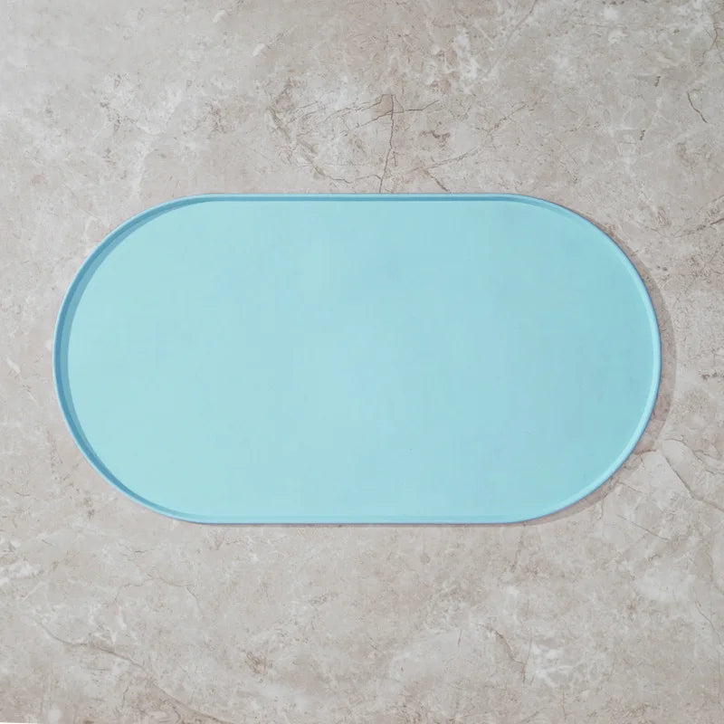 A light blue, oval non-slip feeding mat placed on a beige stone surface.
