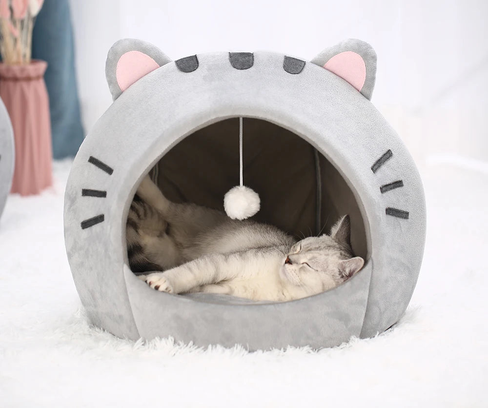 Lit de grotte gris pour chat avec des oreilles roses et un intérieur sombre, montrant un chaton endormi.
