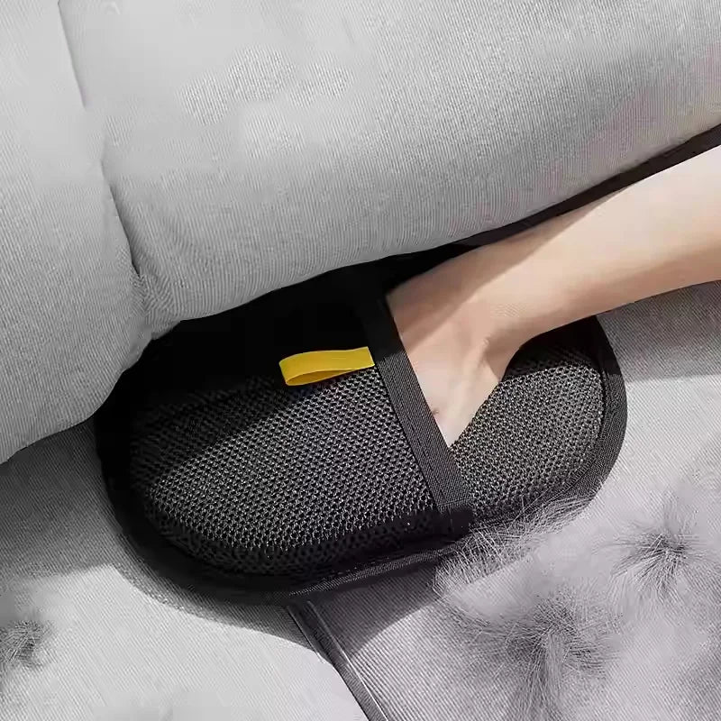 A hand wearing a black reusable pet grooming glove with a yellow accent is resting on a light gray fabric surface.
