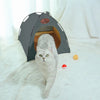 A fluffy gray cat is looking out of a dark gray foldable outdoor cat tent on a white, furry surface.