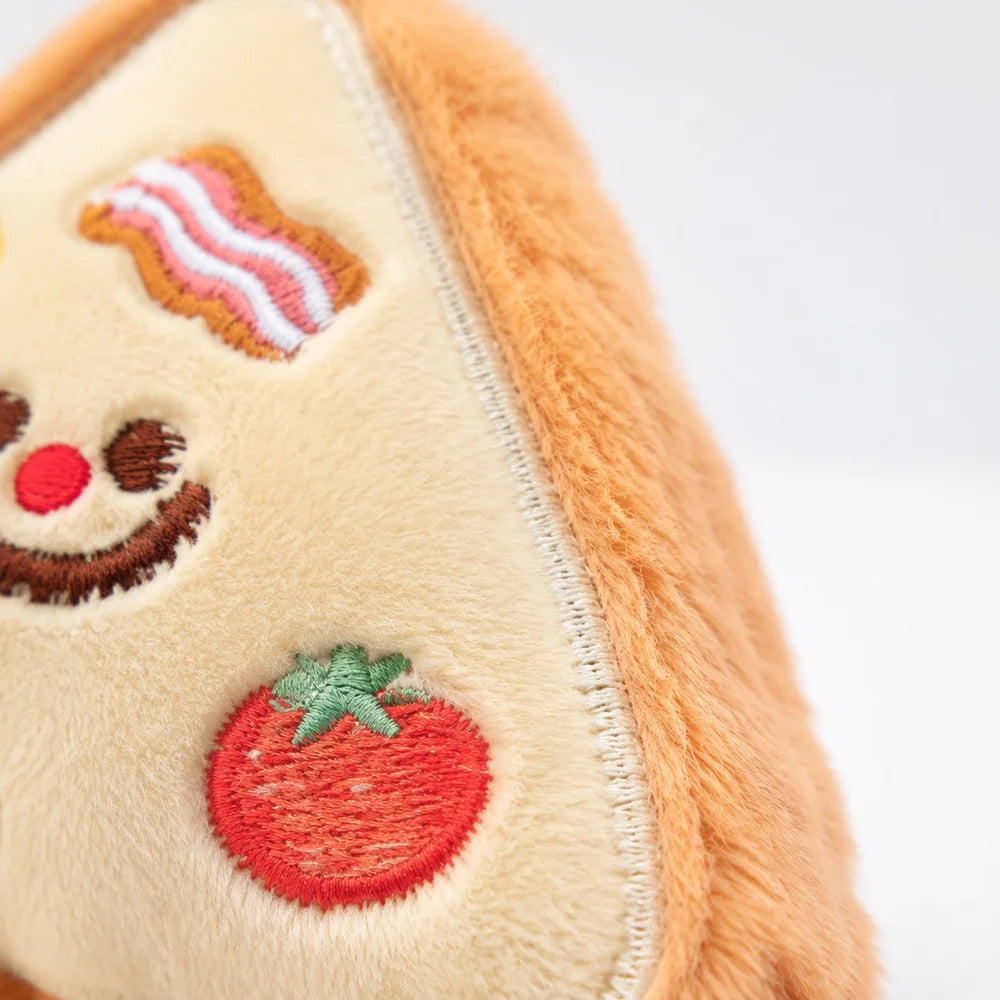Close-up of a light yellow plush toy shaped like a dog's head with embroidered features and a strawberry detail.