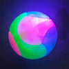 A glowing rubber fetch ball for dogs, illuminated with vibrant pink, green, and blue light.