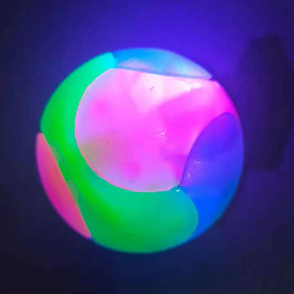 A glowing rubber fetch ball for dogs, illuminated with vibrant pink, green, and blue light.