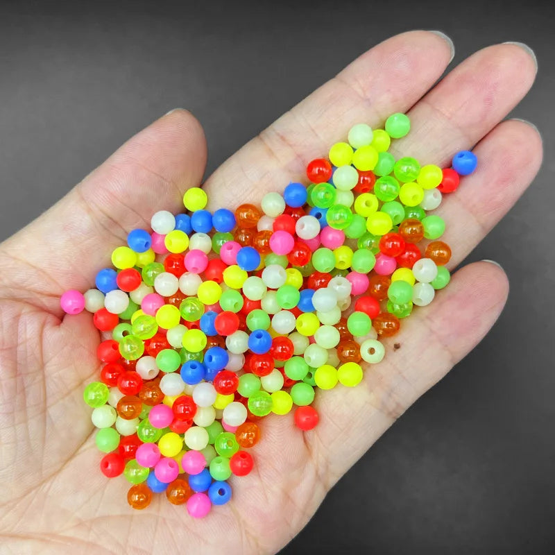 A hand holds a large pile of mixed glow-in-the-dark fishing beads in various bright colors.