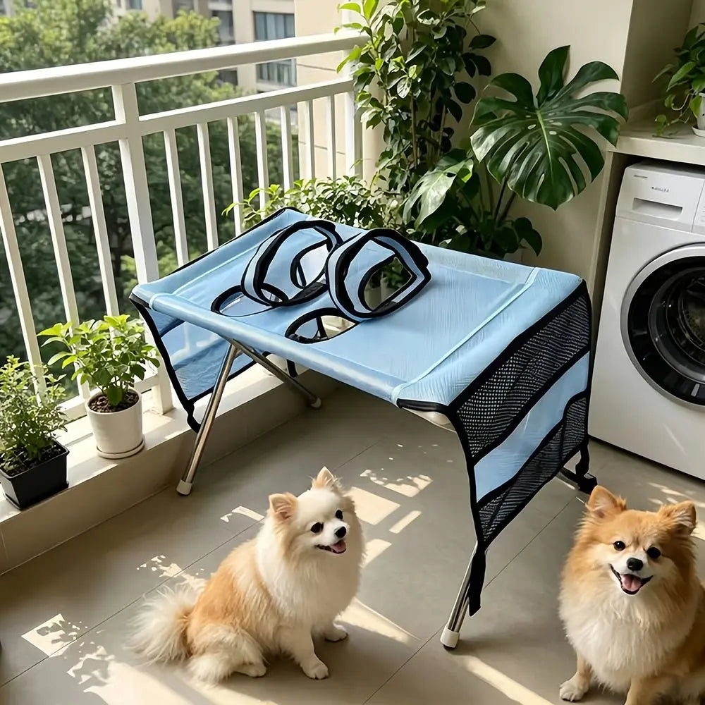 A fluffy white dog is sitting on a blue pet grooming hammock placed on a balcony railing.