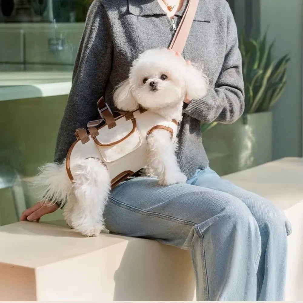 A person is holding a white fluffy dog in a beige portable pet carrier sling bag while sitting down.