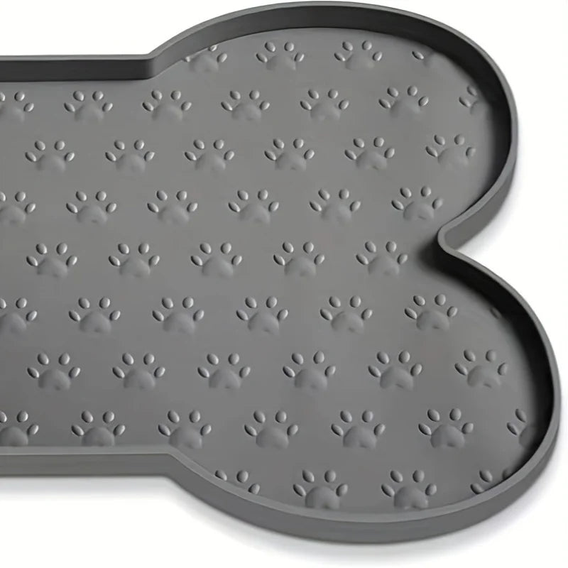 A gray non-slip silicone dog feeding mat with raised edges featuring a pattern of paw prints.