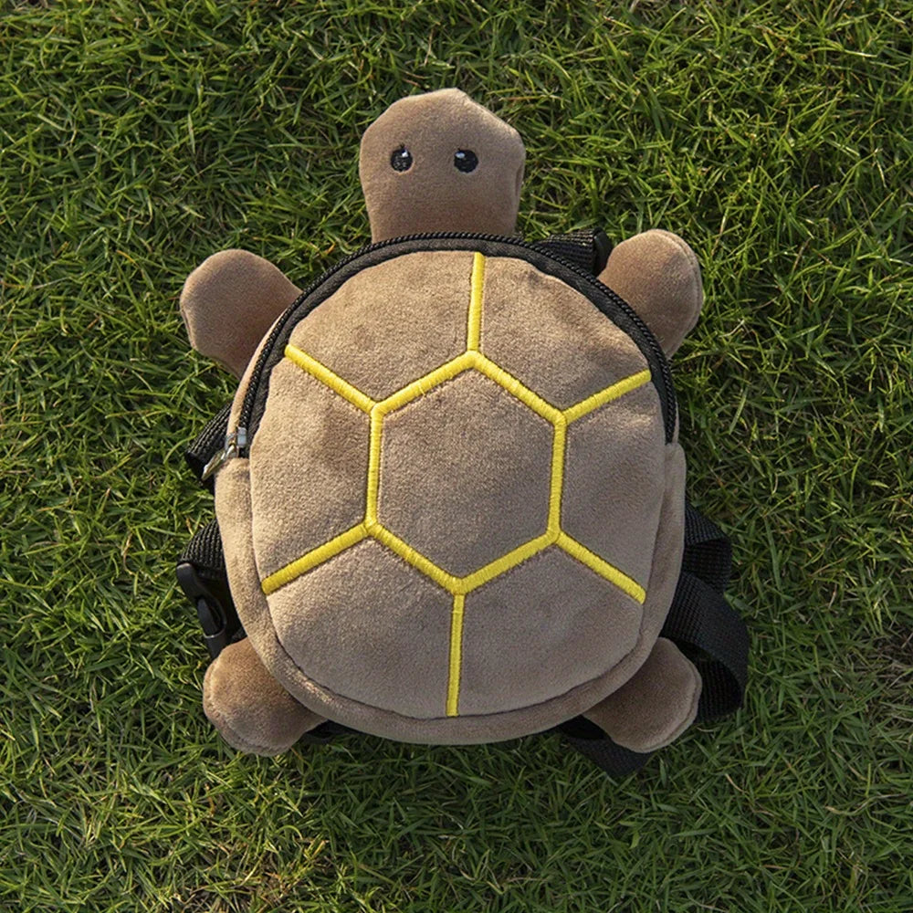 A tan, turtle-shaped pet backpack with a yellow geometric pattern rests on green grass.