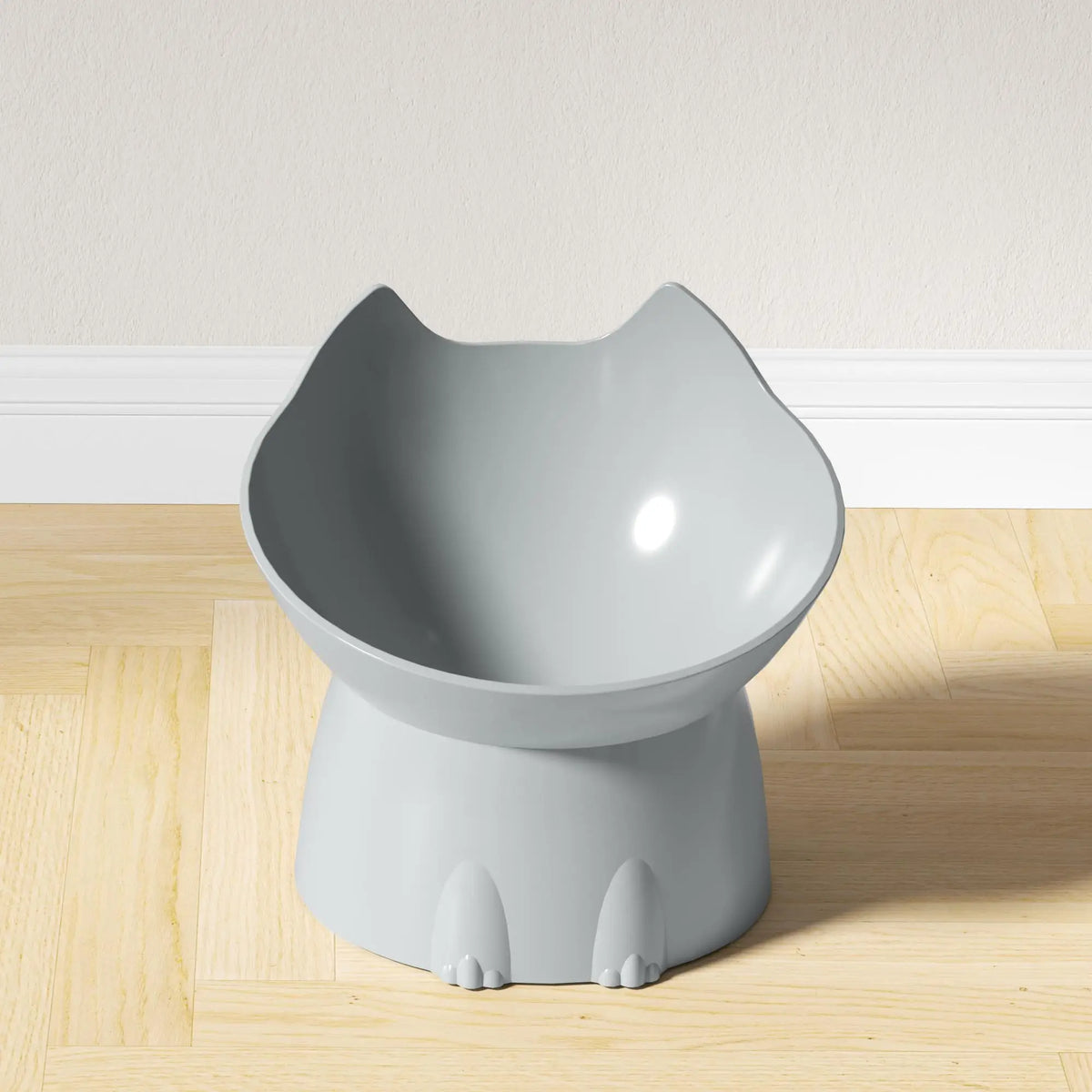 A gray elevated cat bowl with a storage and anti-tip base sitting on a wooden floor.